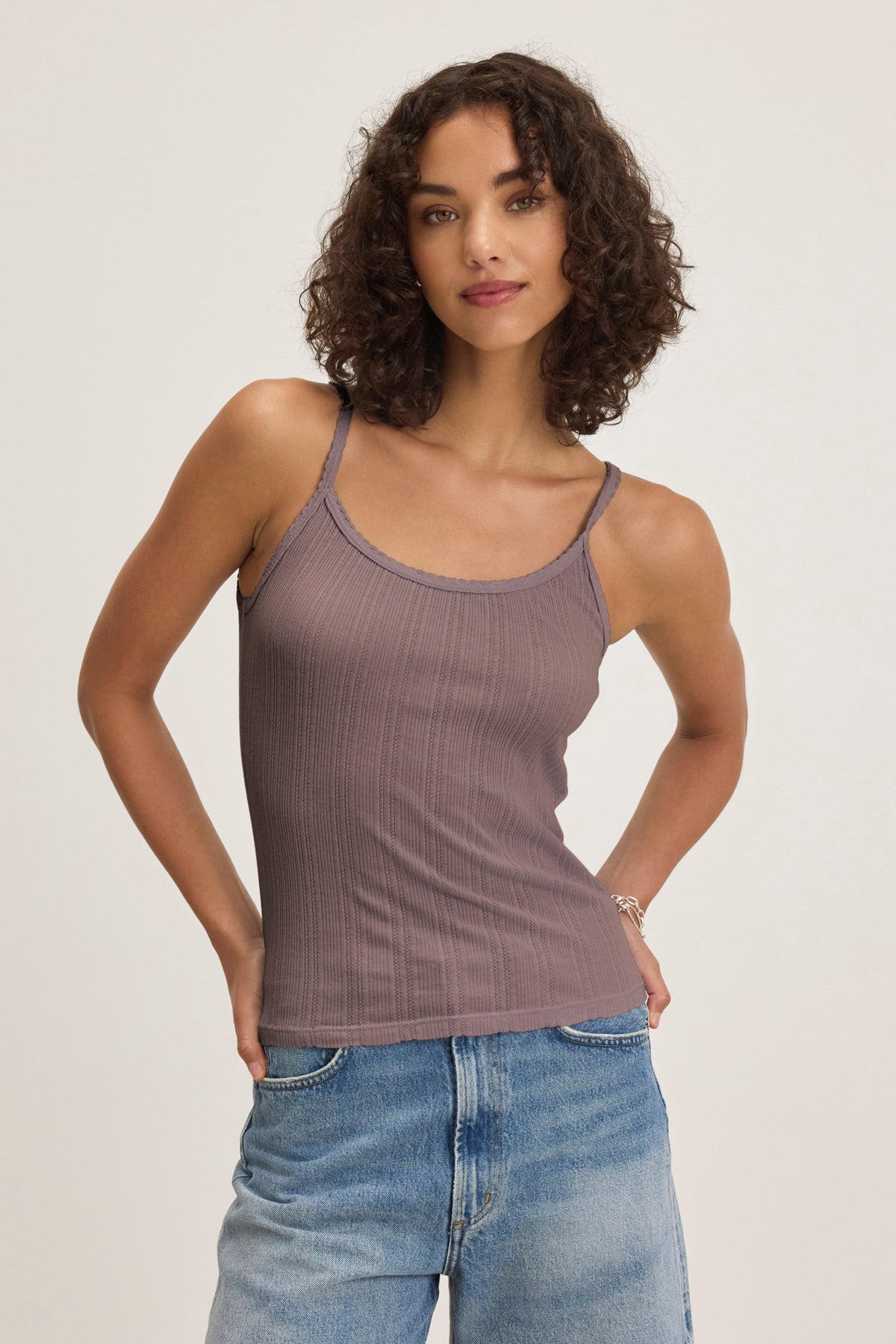 A woman with curly hair wears the Velvet by Graham & Spencer INIKU POINTELLE TANK TOP in mauve and blue jeans, standing against a plain light background.-39173124030657