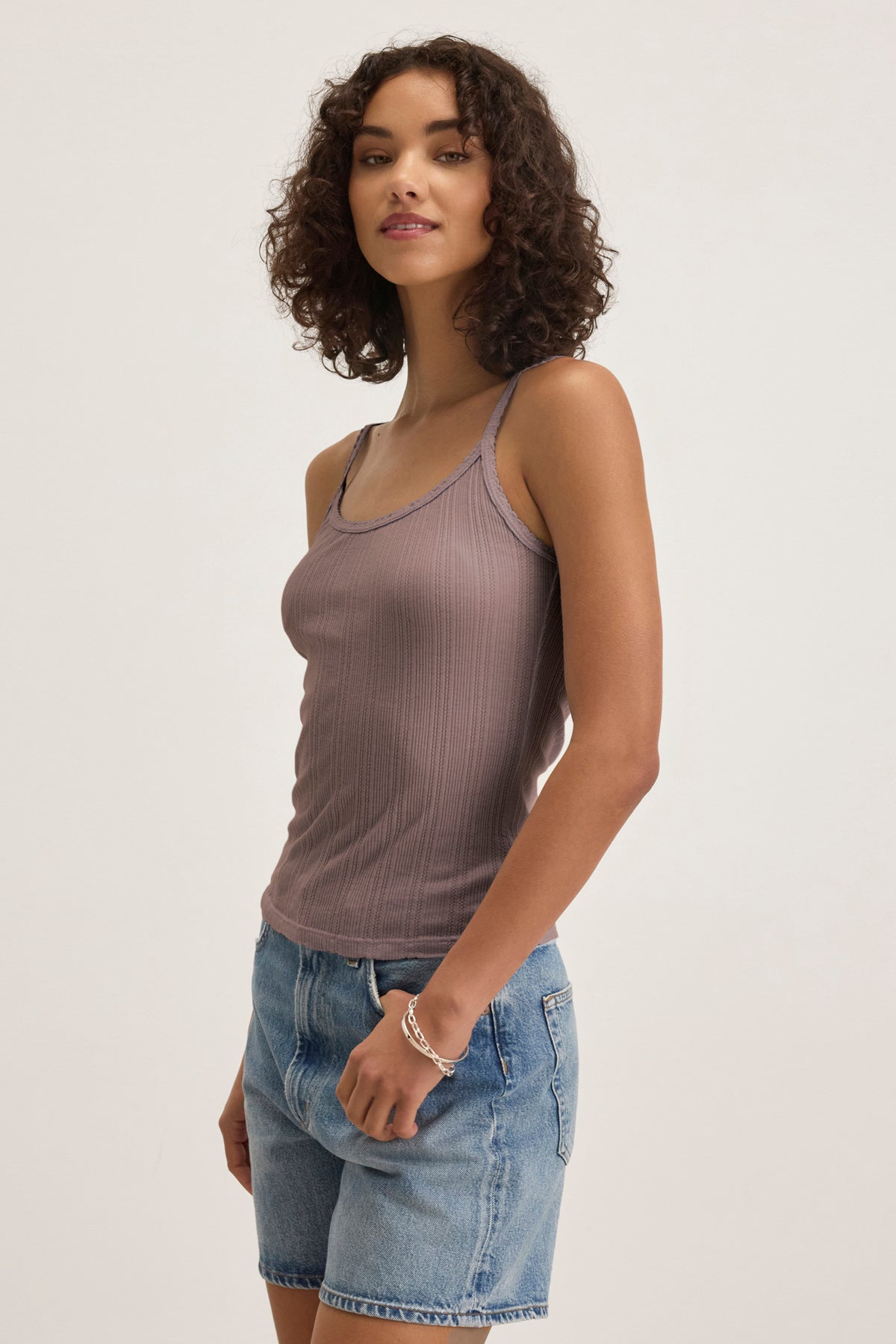 A woman with curly hair wears the Velvet by Graham & Spencer INIKU POINTELLE TANK TOP in mauve and denim shorts, standing against a plain light background.-39173124063425