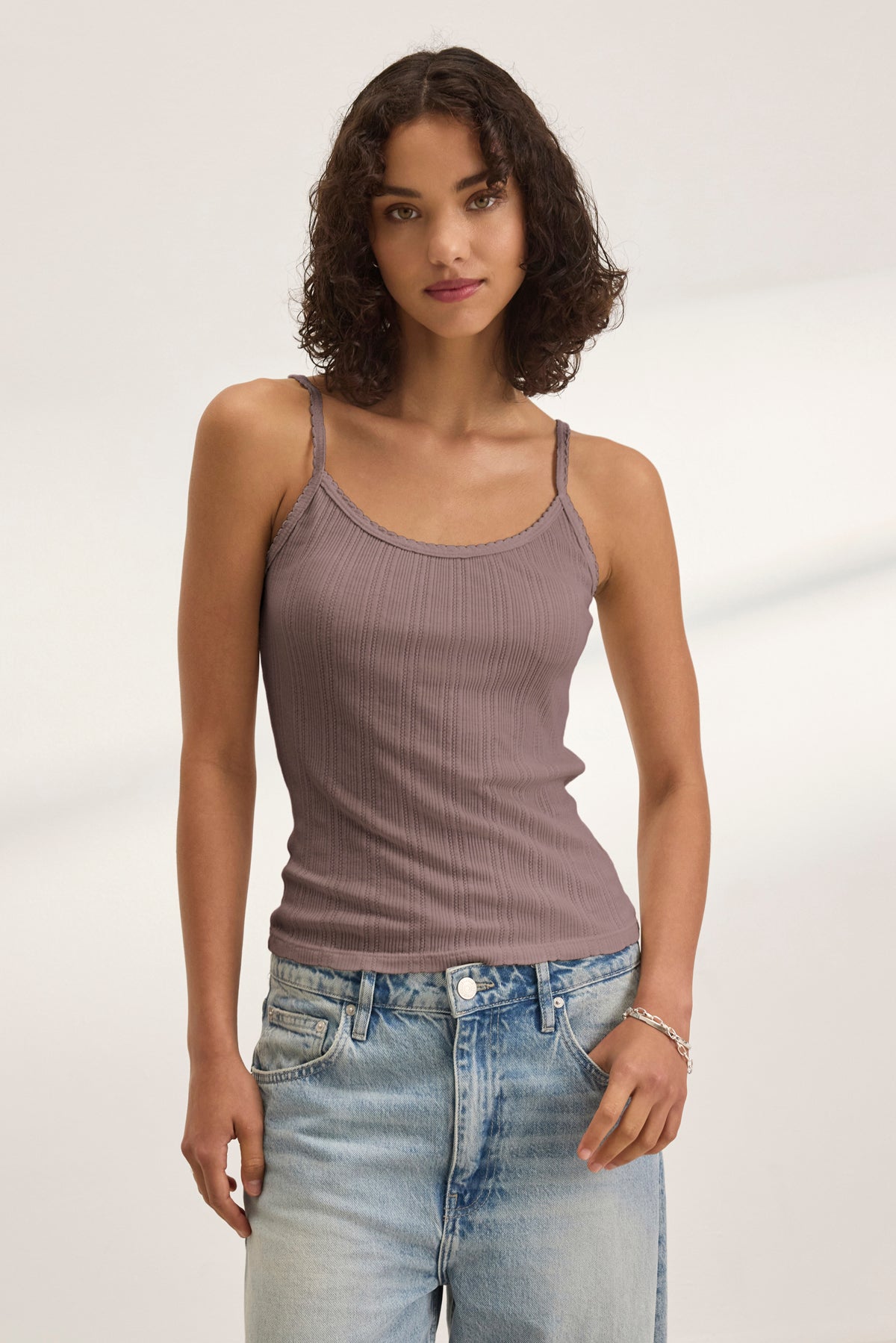 A woman with curly hair wears the INIKU POINTELLE TANK TOP by Velvet by Graham & Spencer in mauve and light blue jeans, standing against a neutral background.-39173124096193