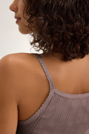 A person with curly dark hair is shown from the side and back, wearing the INIKU POINTELLE TANK TOP by Velvet by Graham & Spencer—a mauve, thin-strapped tank with a pointelle ribbed texture.