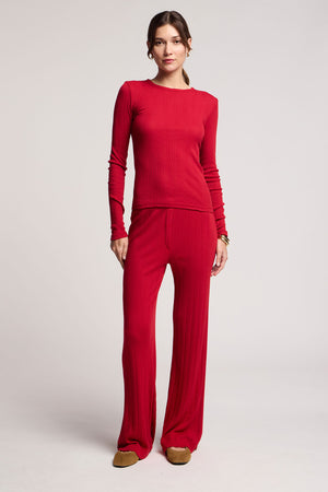 A woman faces forward in the MAURI POINTELLE TEE by Velvet by Graham & Spencer with a scalloped neckline, matching wide-leg pants, and brown slippers, set against a plain light background.