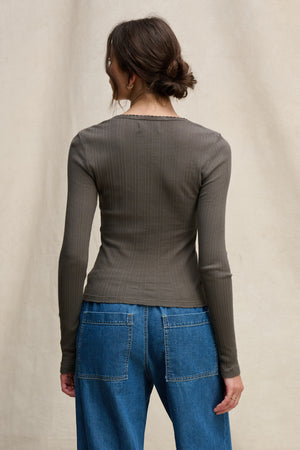 A person with brown hair in a loose bun is shown from the back wearing the WINONA POINTELLE HENLEY by Velvet by Graham & Spencer and blue jeans against a neutral background—a feminine everyday layer.