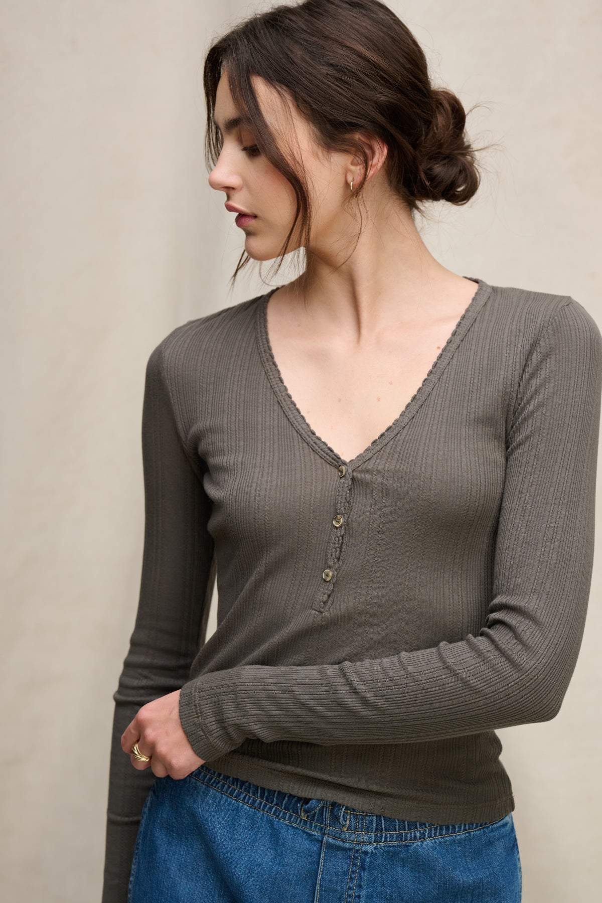 A woman with brown hair in a low bun wears the WINONA POINTELLE HENLEY by Velvet by Graham & Spencer, styled with blue jeans, standing against a neutral background.-39742399217857