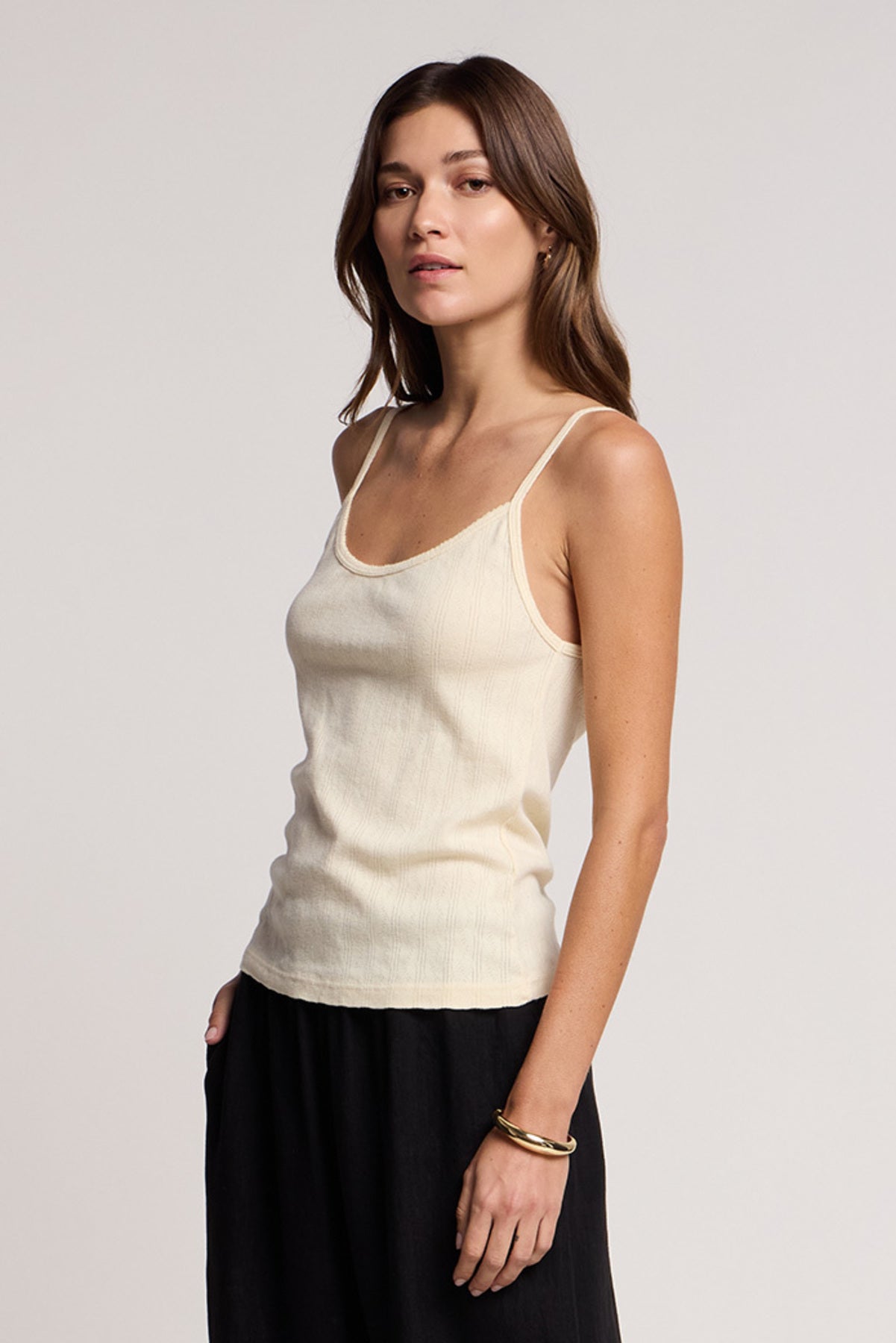 A woman with long brown hair wears the LYNN TANK TOP by Velvet by Graham & Spencer, cream-colored cotton, paired with a black skirt and standing against a plain light background.-41527194681537