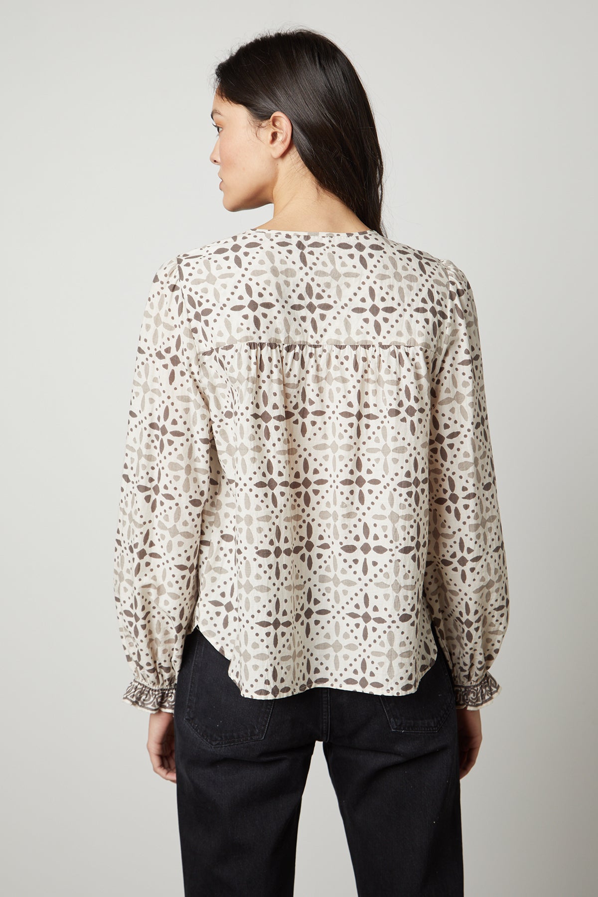   The back view of a woman wearing the Velvet by Graham & Spencer AUDETTE PRINTED BOHO TOP with a geometric pattern in earth tones. 