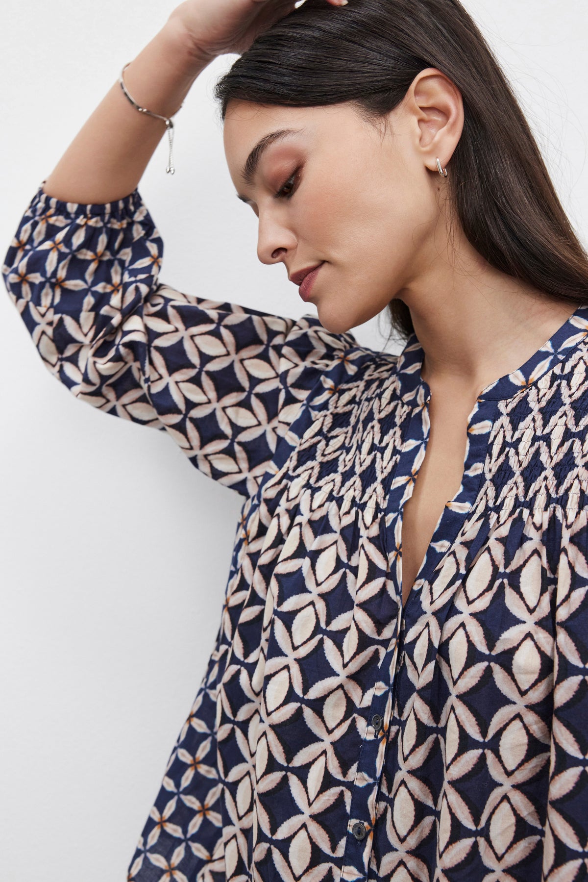   A person with long dark hair is seen in a side profile, wearing the Velvet by Graham & Spencer HADDON TOP with smocked details, with their hand resting on their head. 