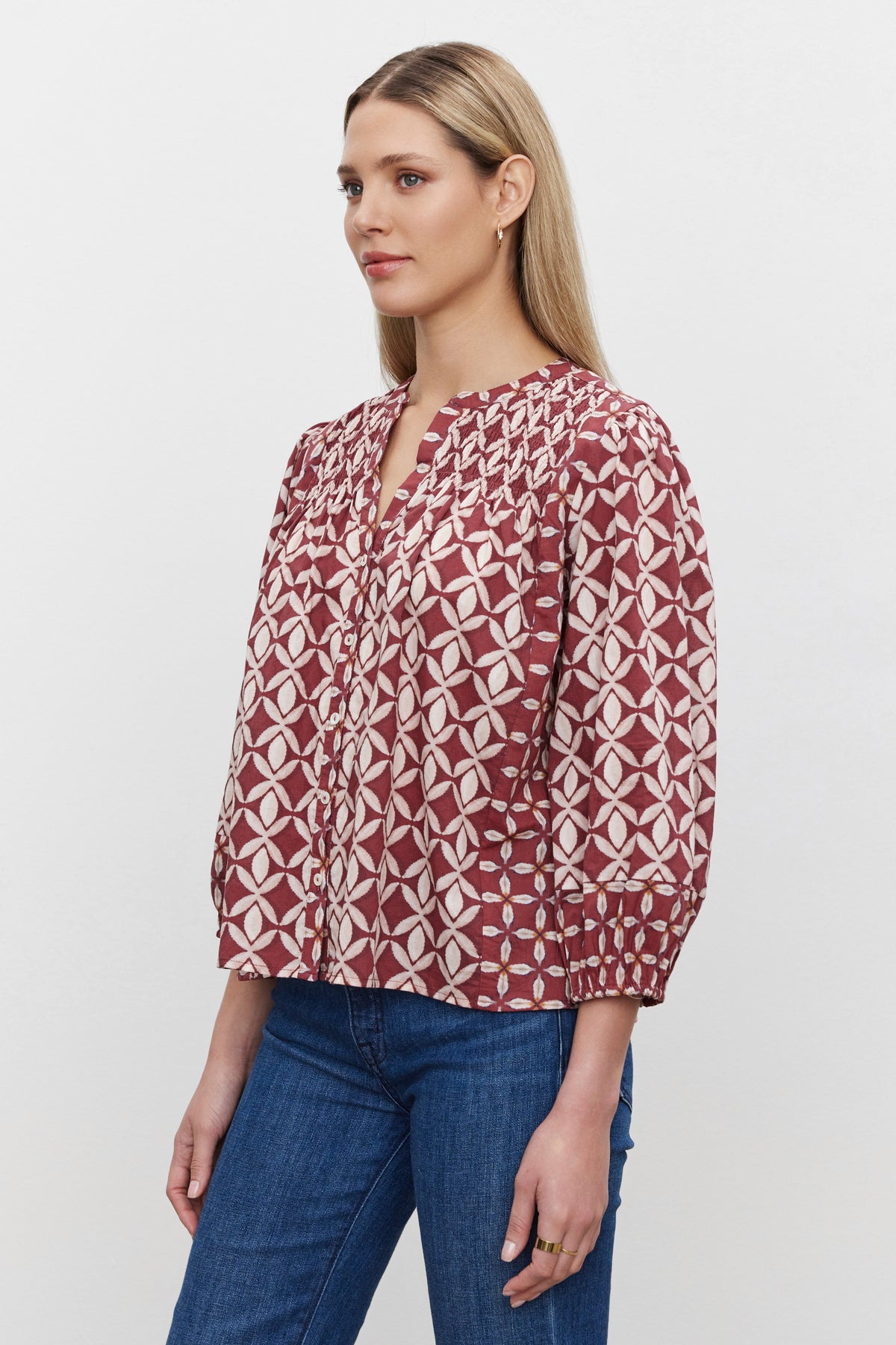   A woman with long blonde hair, exuding casual refinement in the HADDON TOP by Velvet by Graham & Spencer and blue jeans, stands against a plain white background. 