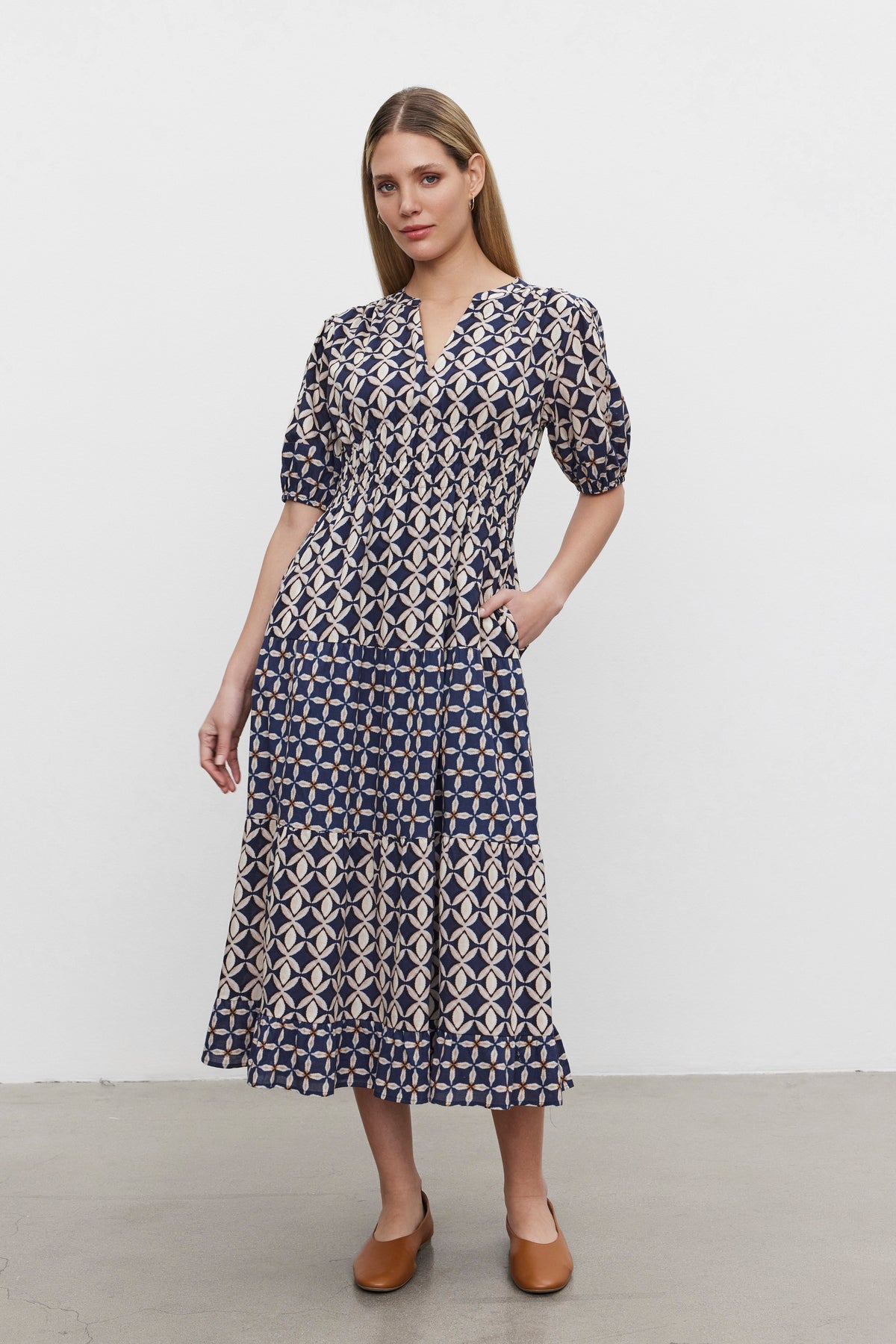   A woman stands against a plain white background wearing the JOEY DRESS, a blue and white printed cotton cambric dress with a v-neckline and short sleeves by Velvet by Graham & Spencer, paired with brown shoes. 