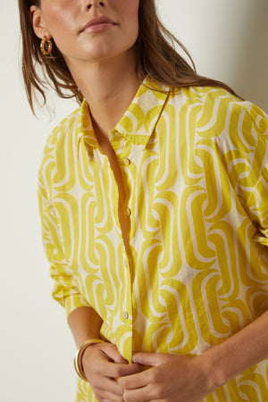 a woman wearing a yellow ANNALISE PRINTED TOP with a geometric pattern by Velvet by Graham & Spencer.