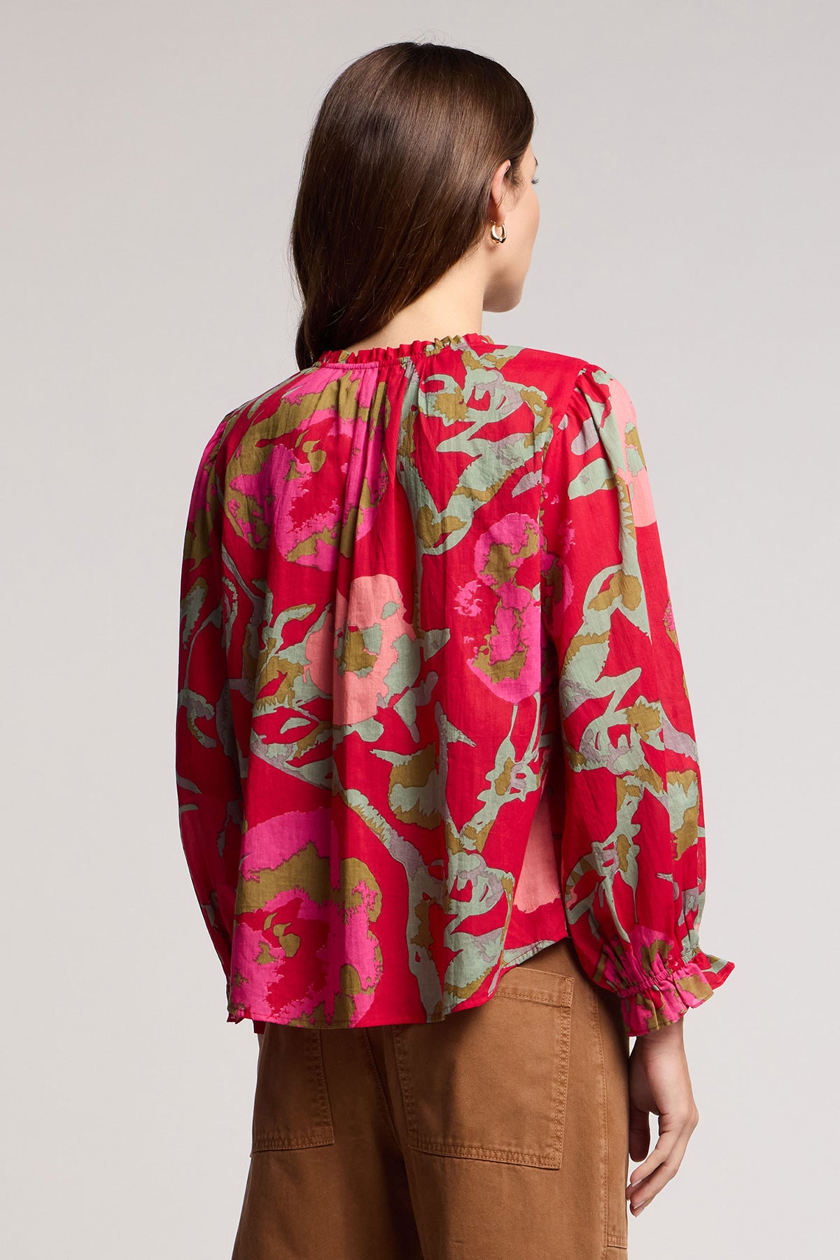 Woman with long brown hair, seen from the back, wears the AVENA TOP by Velvet by Graham & Spencer—a red floral blouse with green and pink patterns—paired with brown pants.-41588174192833