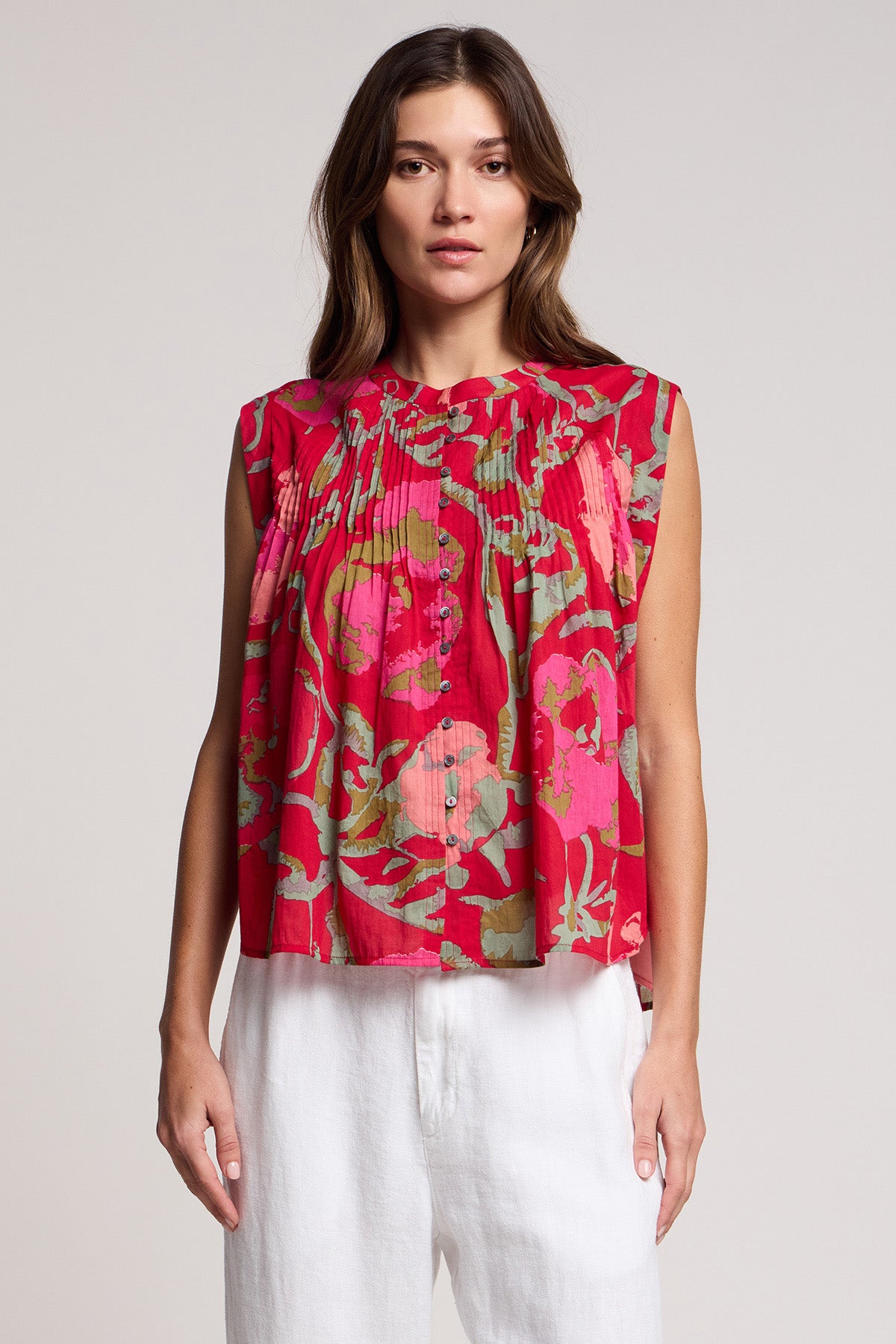 A woman wears the JEANNE TOP by Velvet by Graham & Spencer—a romantic sleeveless rose vine blouse with pleats—paired with white pants, standing against a plain light background.