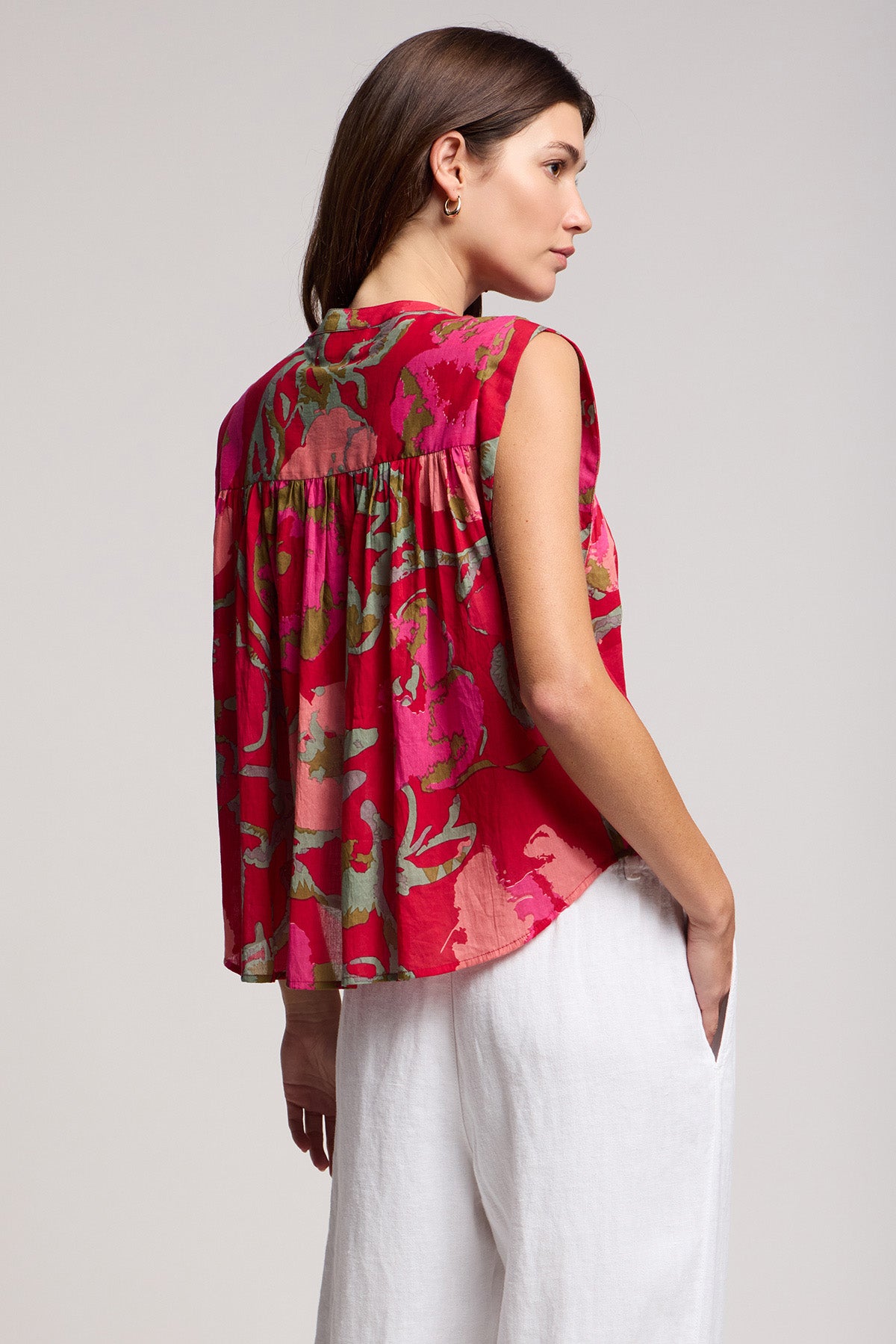 A woman stands sideways in the Velvet by Graham & Spencer JEANNE TOP and white pants, one hand in her pocket, gazing to the side.