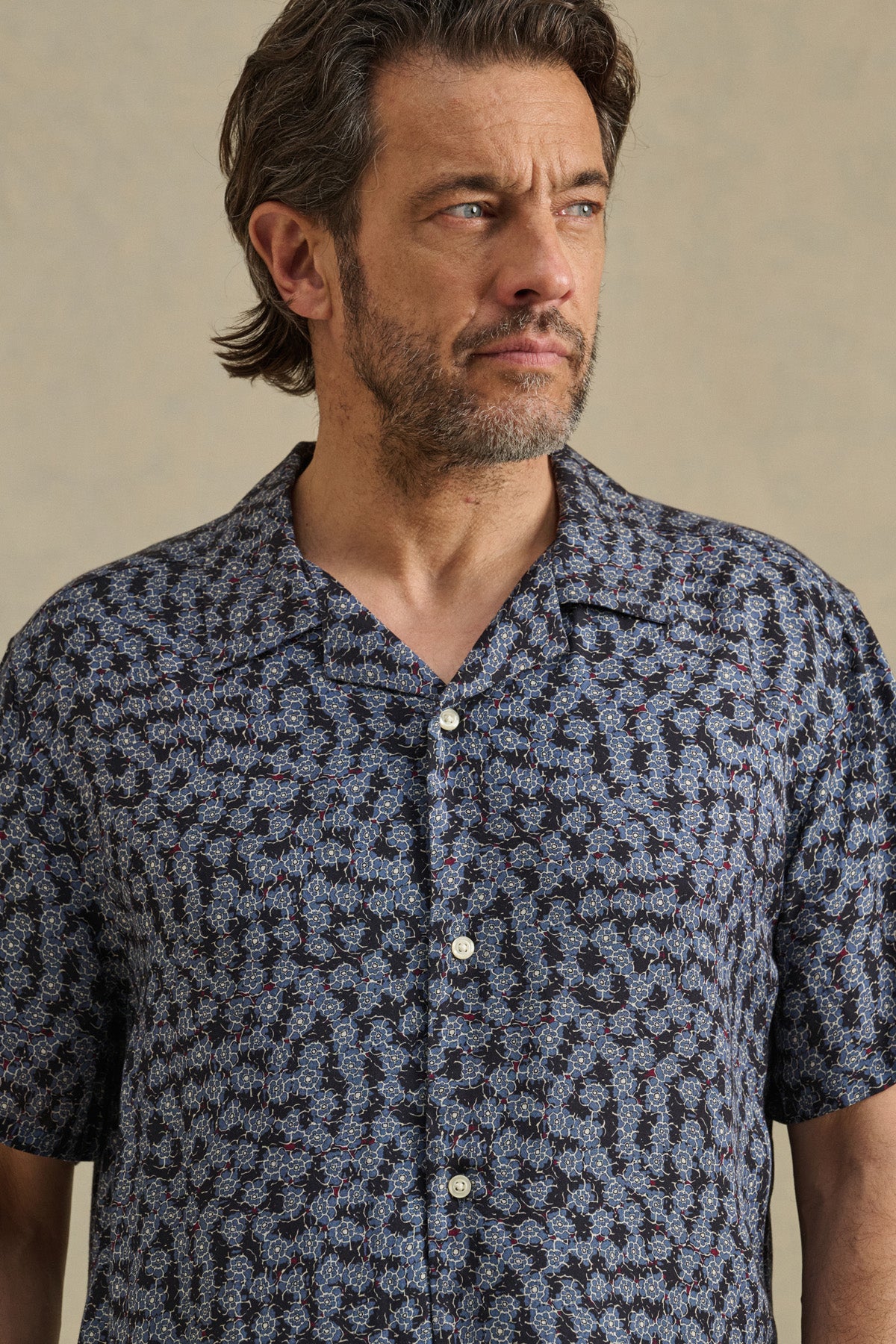 A man with medium-length brown hair and a beard wears the EMILIO SHIRT by Velvet by Graham & Spencer, a short-sleeve camp collar shirt in breathable modal, while looking to the side against a neutral background.-41428141506753