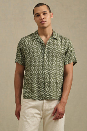 A man wearing the EMILIO SHIRT by Velvet by Graham & Spencer, a breathable modal button-up with relaxed fit and camp collar, paired with light-colored pants, stands against a neutral background.