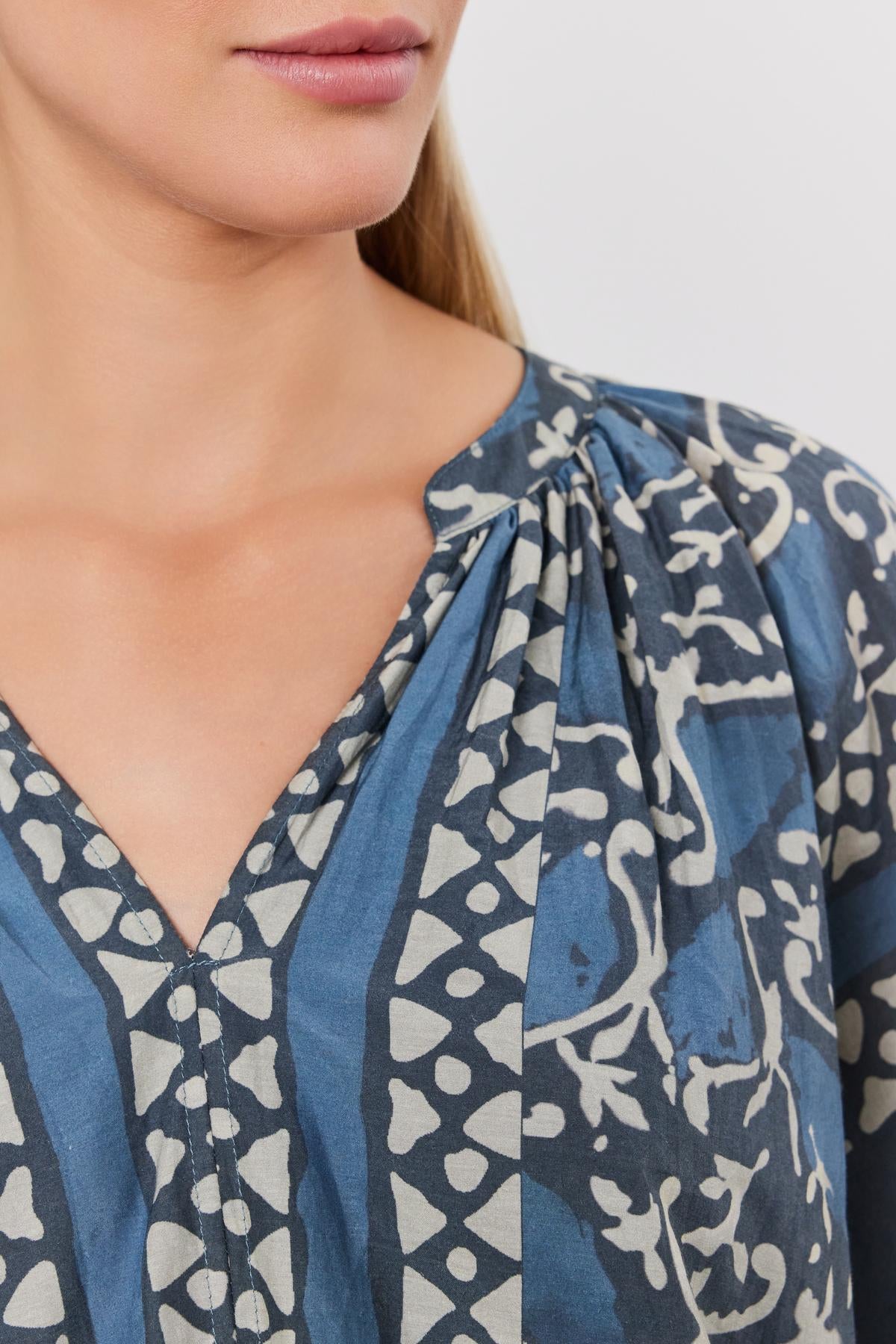   Close-up of a woman wearing a blue and white printed silk cotton voile Dayana Top by Velvet by Graham & Spencer with a v-neckline. 