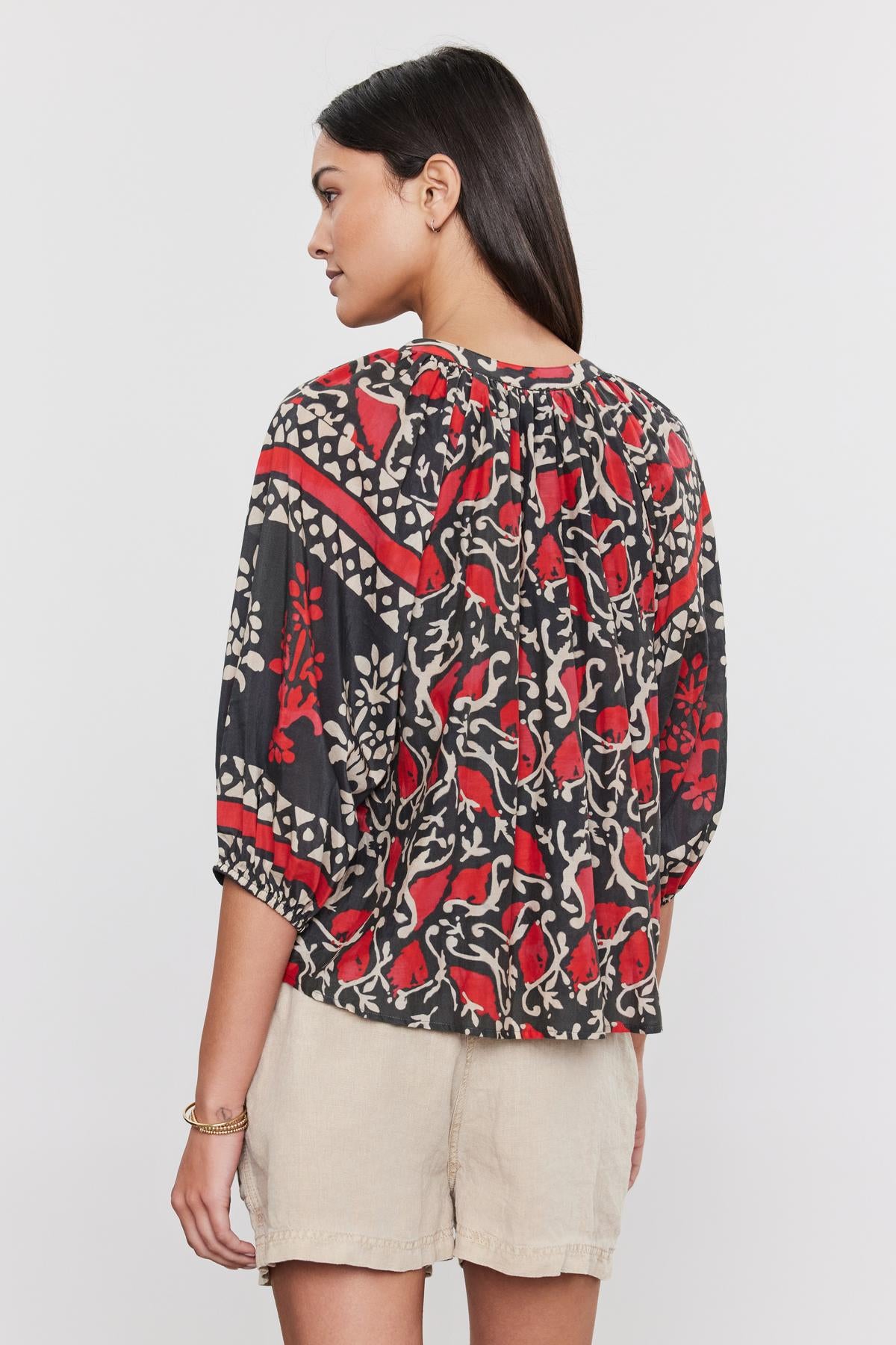   Woman from the back wearing a DAYANA TOP by Velvet by Graham & Spencer with a red, black, and white floral pattern on printed silk cotton voile, paired with beige shorts. 