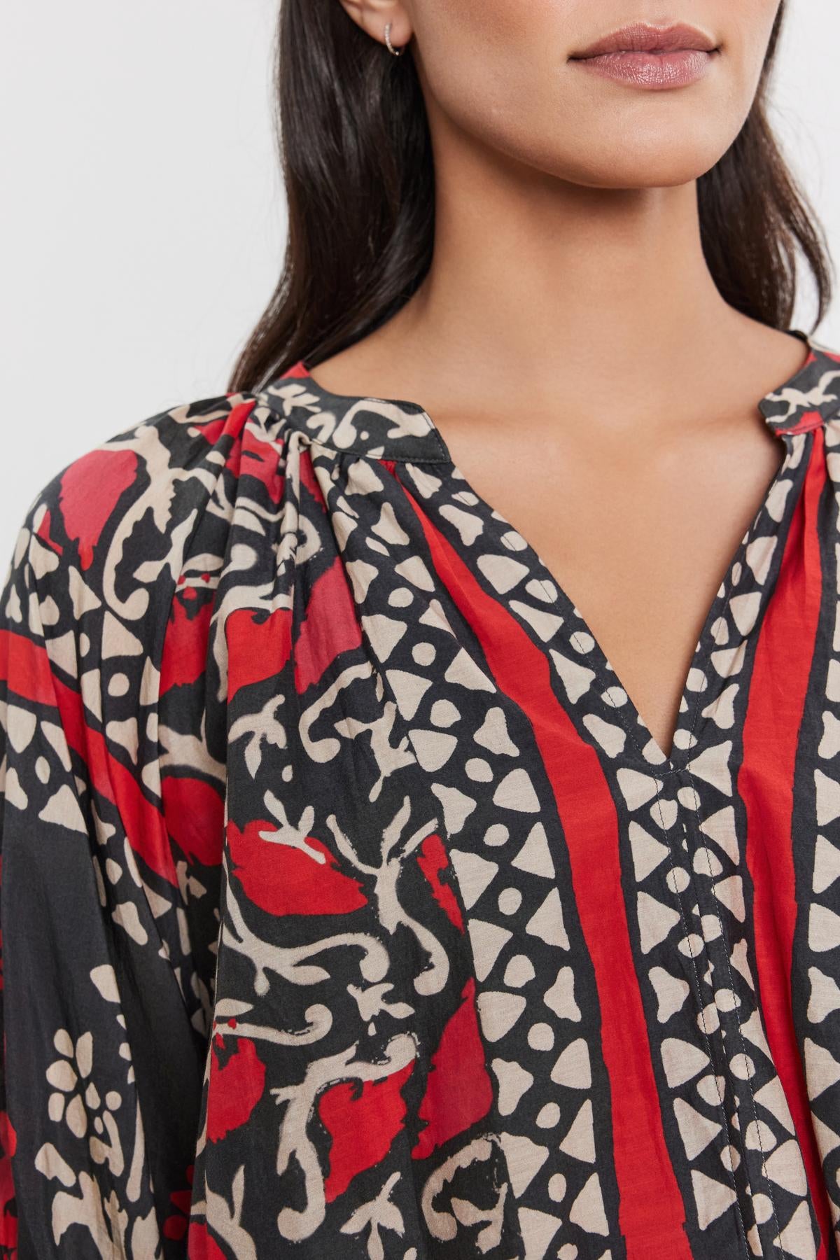   Close-up of a woman wearing the DAYANA TOP by Velvet by Graham & Spencer, with a bold red and black floral pattern on printed silk cotton voile, focusing on the detailed neckline. 