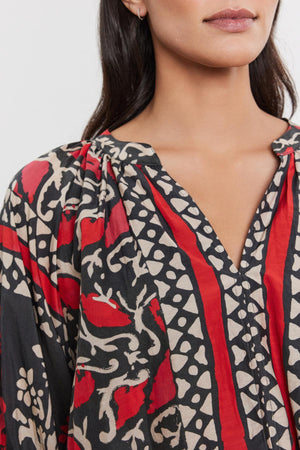 Close-up of a woman wearing the DAYANA TOP by Velvet by Graham & Spencer, with a bold red and black floral pattern on printed silk cotton voile, focusing on the detailed neckline.