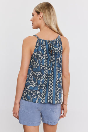 Woman in a blue printed silk cotton voile RHEA TANK TOP with tie straps at the neck, paired with denim shorts, viewed from behind. Brand: Velvet by Graham & Spencer