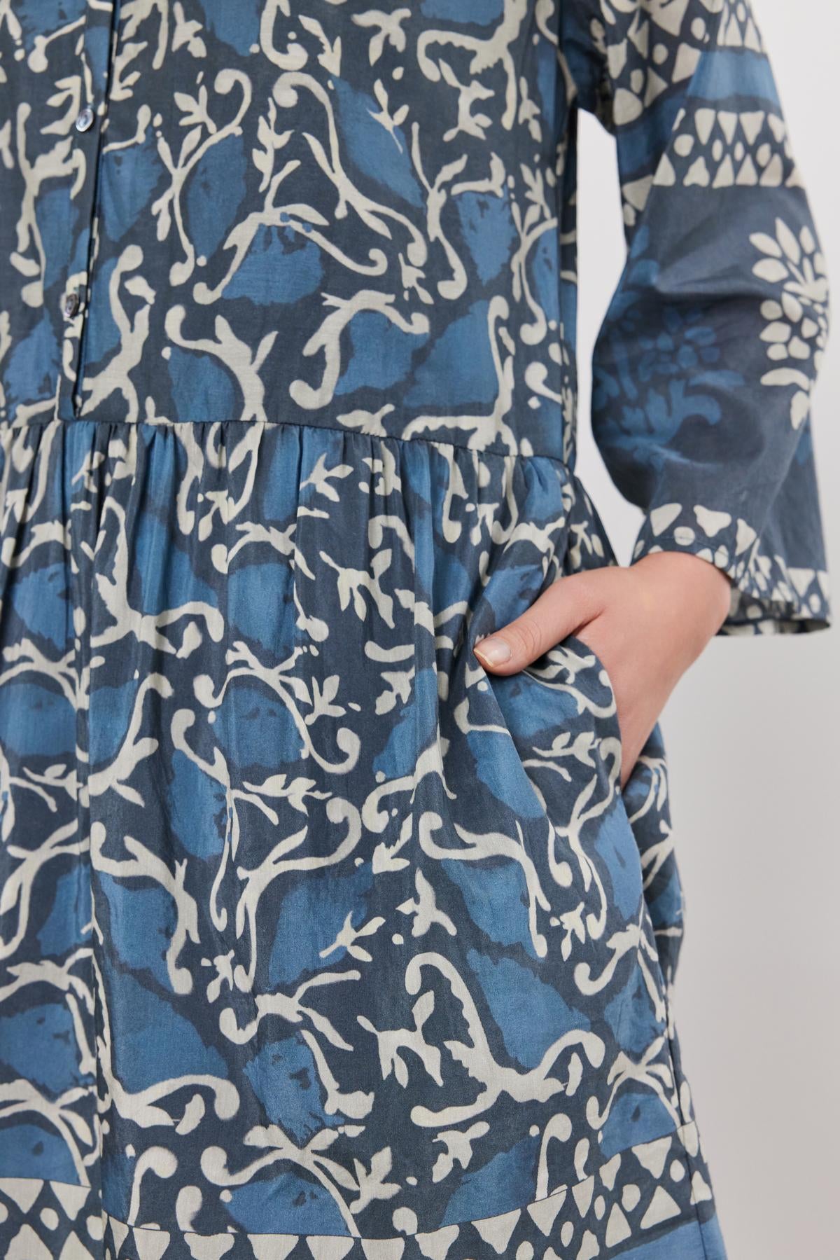   Close-up of a person in a blue and white floral Velvet by Graham & Spencer Talia dress, focusing on the midsection where a hand gently pinches the fabric. 