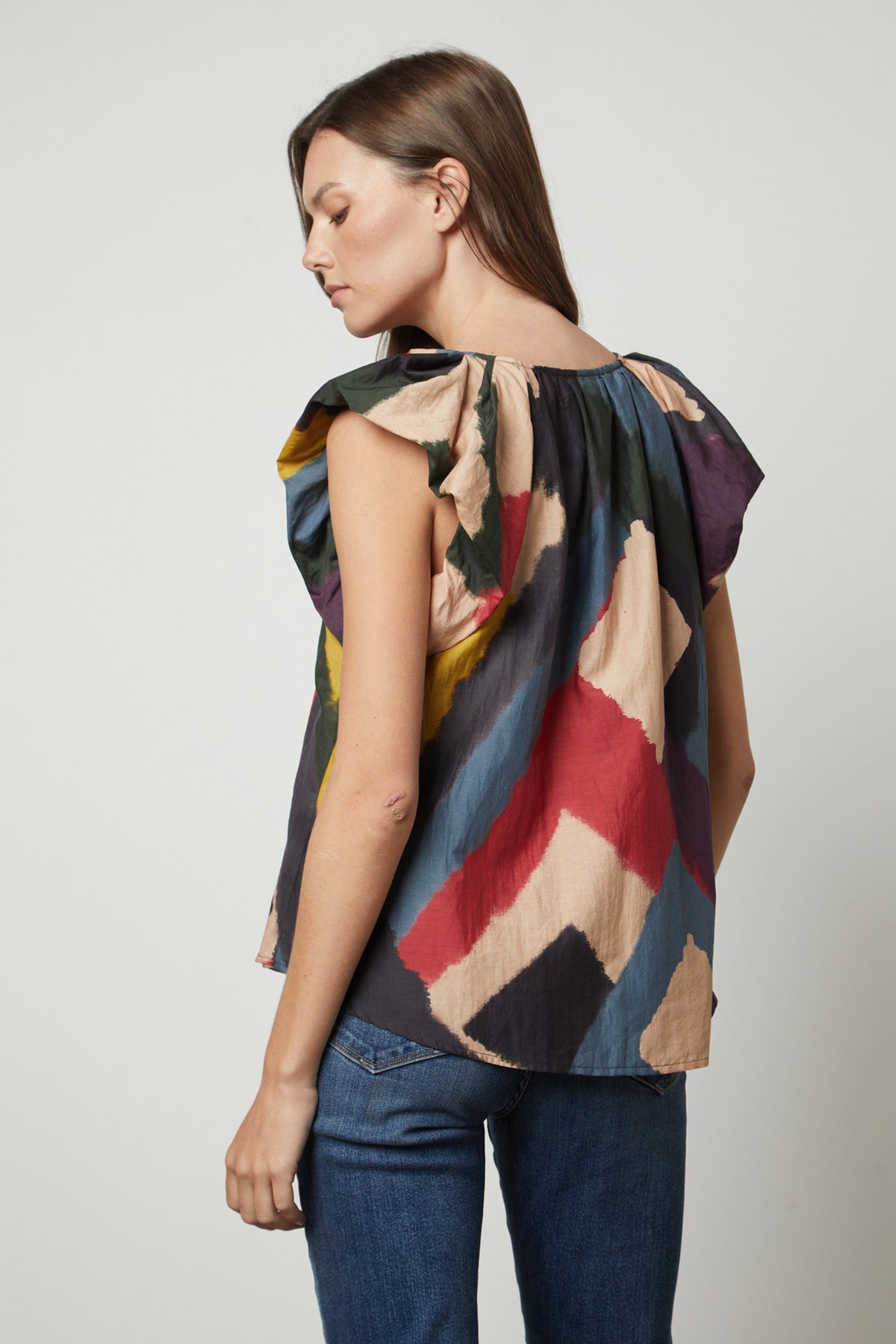   The back view of a woman wearing a Velvet by Graham & Spencer TAMARA PRINTED TOP with flutter sleeves and multi colored design. 