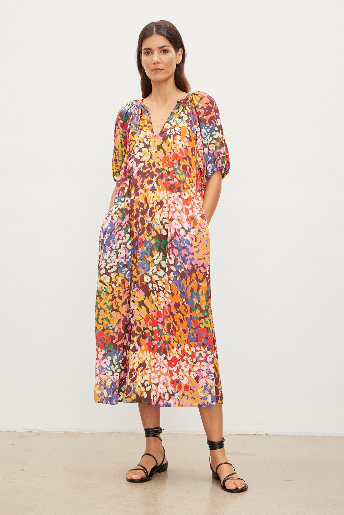   Woman standing in a gallery, wearing a CAROL PRINTED BOHO DRESS by Velvet by Graham & Spencer and black sandals, looking directly at the camera. 