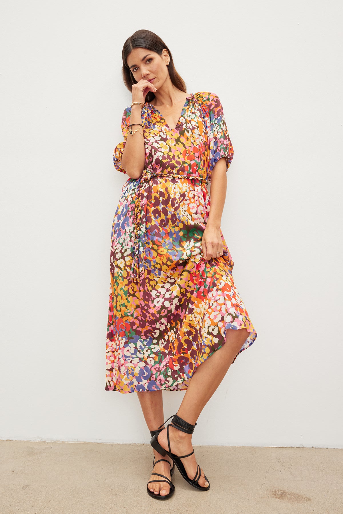   Woman in a CAROL PRINTED BOHO DRESS by Velvet by Graham & Spencer and black sandals, standing against a white background, gently touching her face while looking at the camera. 