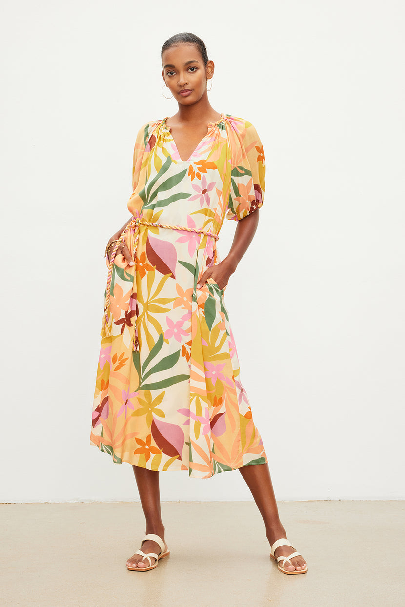 A woman standing, wearing a colorful floral printed CAROL BOHO DRESS by Velvet by Graham & Spencer and beige sandals, with her hands gently resting on her hips.