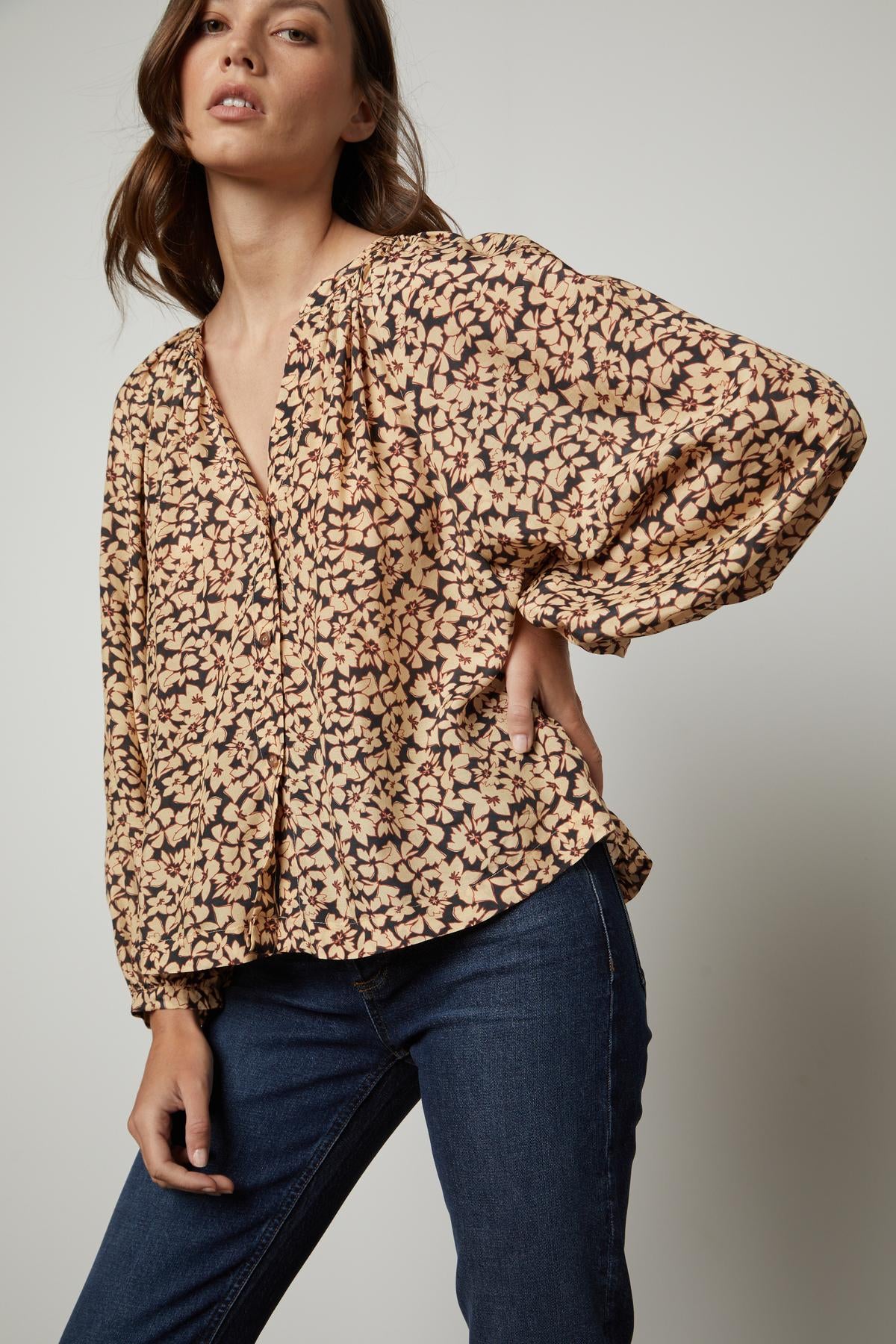 The model is wearing jeans and a MELINDA PRINTED BUTTON-UP TOP by Velvet by Graham & Spencer with a floral print.-26895474426049