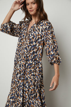 The model is wearing a blue and brown button front Velvet by Graham & Spencer OTTILIE PRINTED BOHO DRESS.