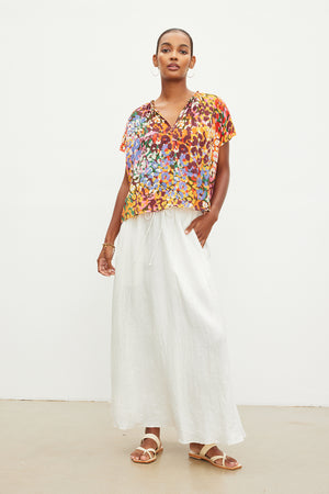 The model is wearing a floral top and white wide leg pants made from woven linen fabric.