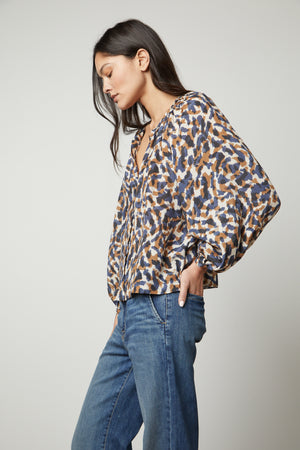 The model is wearing jeans and a printed button-up top.