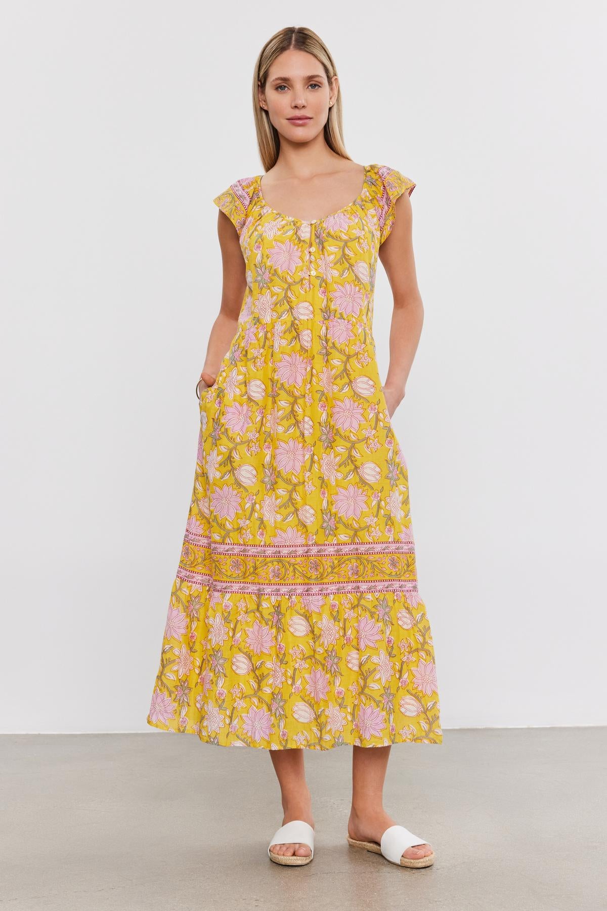   A woman stands against a plain white background, wearing the JAZLYN DRESS from Velvet by Graham & Spencer and white sandals. Her hands are in her dress pockets, making it a perfect addition to any summer wardrobe. 