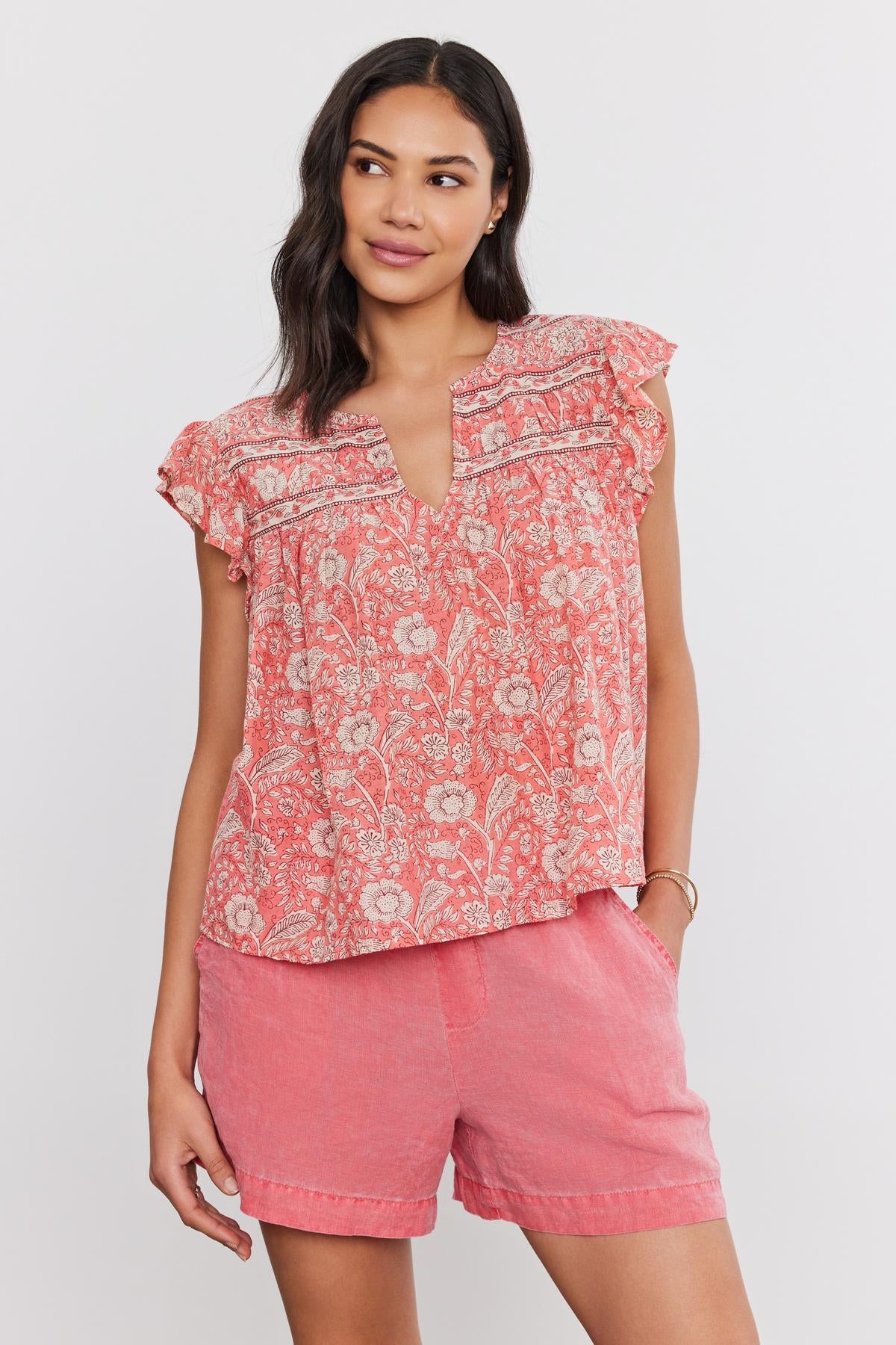 A woman wearing a coral Velvet by Graham & Spencer Kenzie Top with floral print and matching shorts, standing against a plain background.-36910087372993