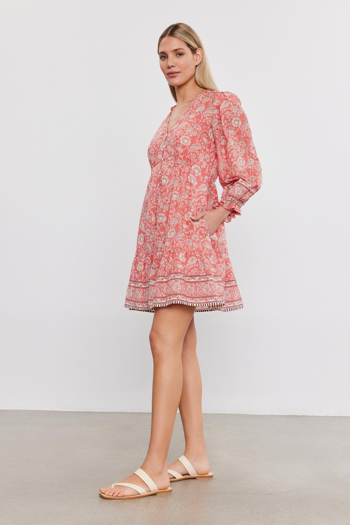 Woman in a floral print cotton voile Velvet by Graham & Spencer MARY DRESS and white sandals standing against a plain background.-36910098874561