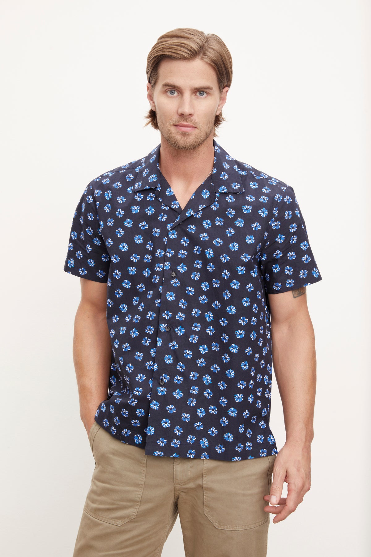  Man wearing a short-sleeved patterned Iggy button-up shirt by Velvet by Graham & Spencer and khaki pants standing against a plain background. 