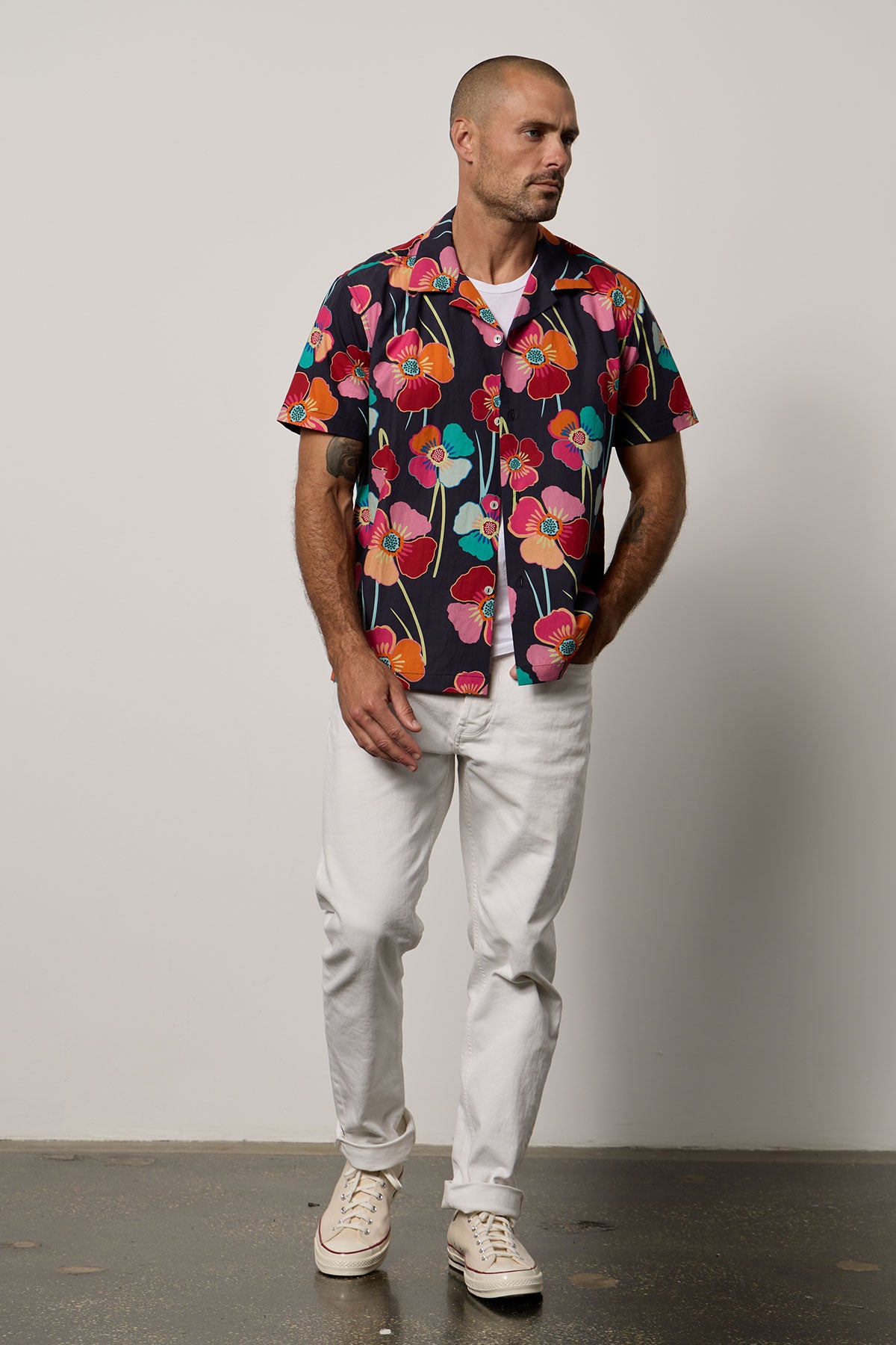 A man wearing a Velvet by Graham & Spencer Iggy printed button-up shirt and white pants, perfect for summer vacations.-35678388158657
