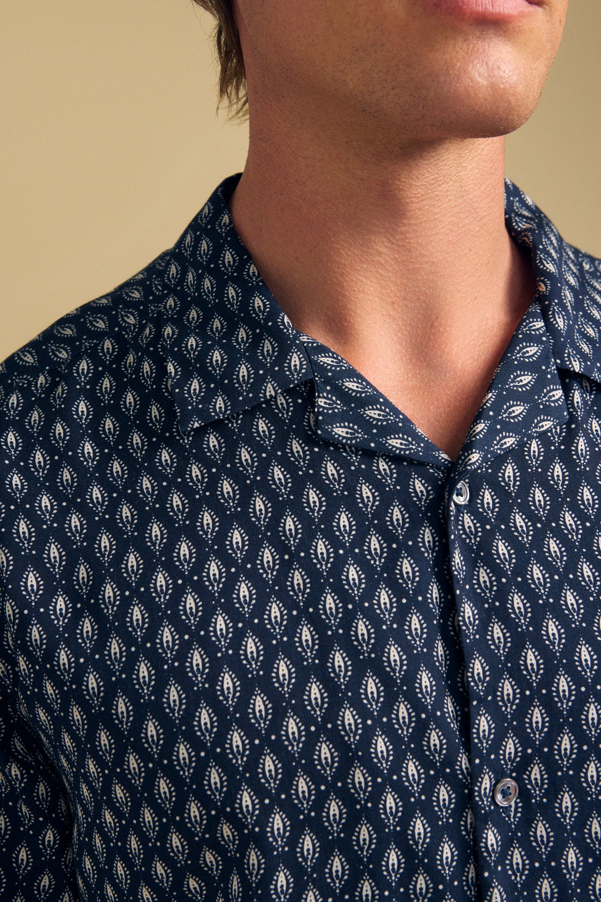 A person wearing the EMILIO SHIRT by Velvet by Graham & Spencer, a relaxed fit navy camp collar shirt with a white geometric leaf pattern, made from breathable modal for all-day comfort. Shown from the shoulders up.