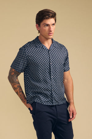 A man with short brown hair and a tattooed arm wears the EMILIO SHIRT by Velvet by Graham & Spencer with dark pants, standing against a plain beige background.
