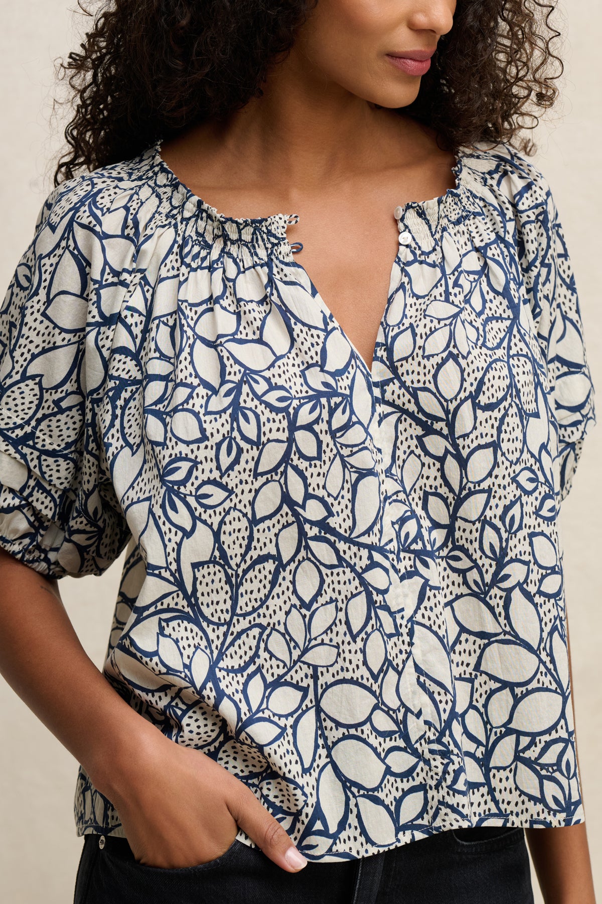 A person wearing the THERA TOP by Velvet by Graham & Spencer, a lightweight cotton voile blouse with blue and white leaf print, short sleeves, smocked neckline, gathered details, and a slight v-cut front.-39539194921153
