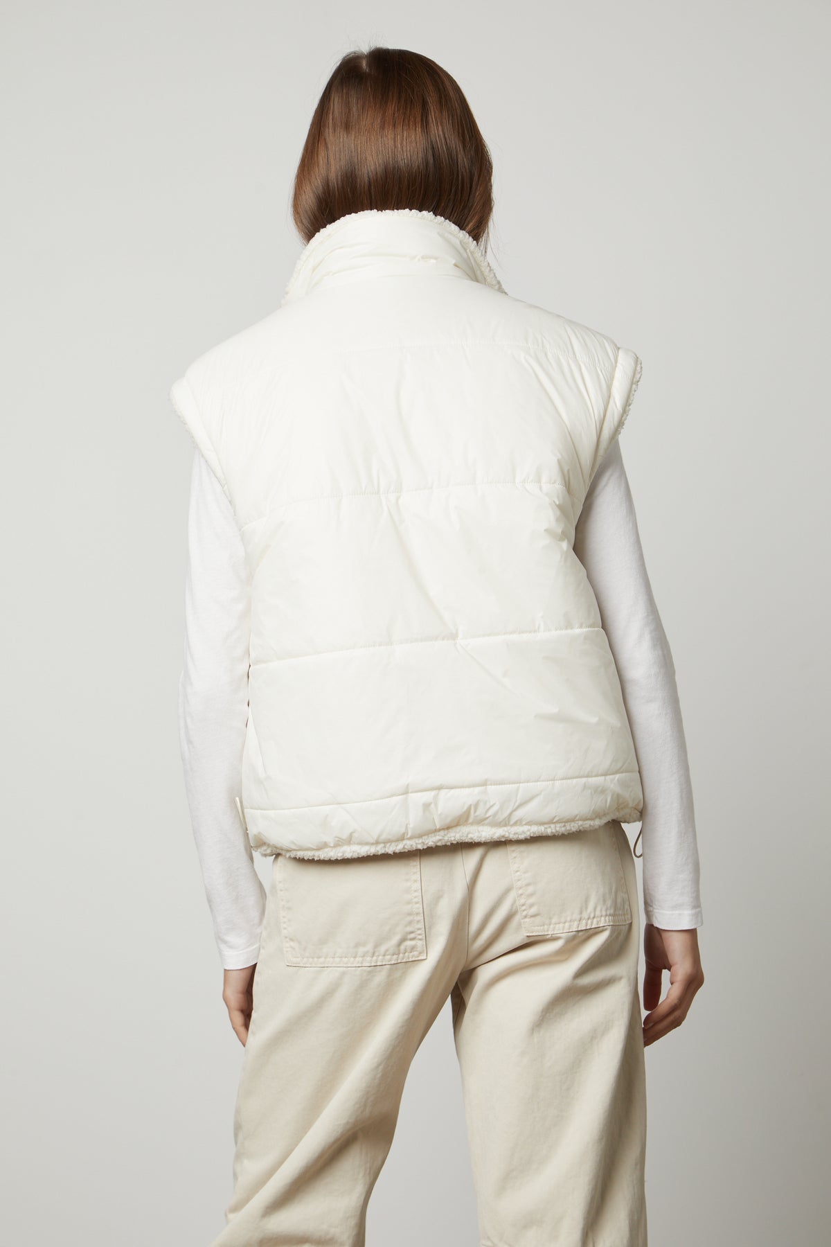   The back view of a woman wearing a white ALICIA REVERSIBLE PUFFER SHERPA VEST by Velvet by Graham & Spencer, perfect for cold weather. 