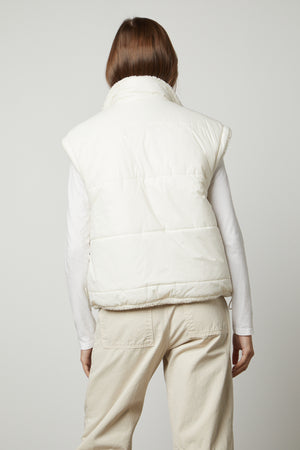 The back view of a woman wearing a white ALICIA REVERSIBLE PUFFER SHERPA VEST by Velvet by Graham & Spencer, perfect for cold weather.