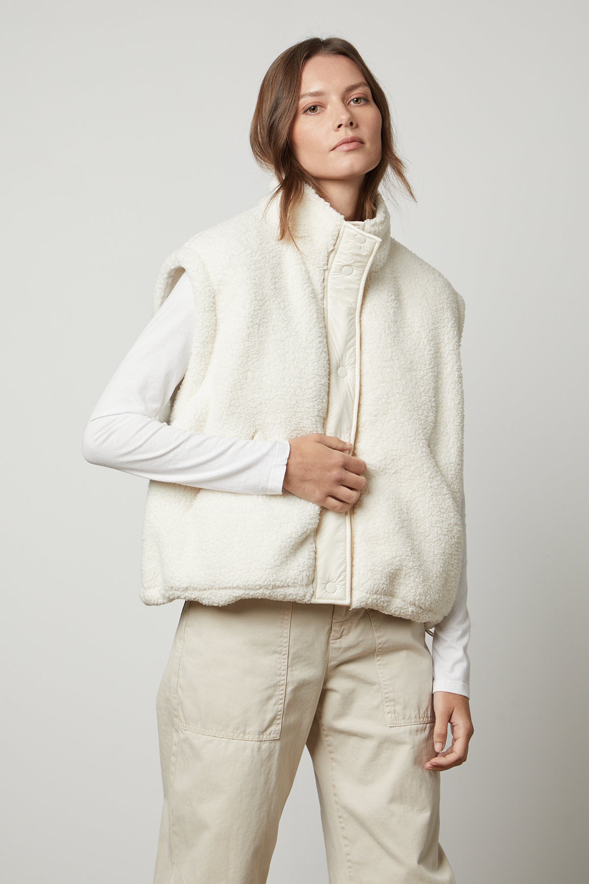   A woman wearing a white Velvet by Graham & Spencer Alicia Reversible Puffer Sherpa Vest designed for cold weather. 