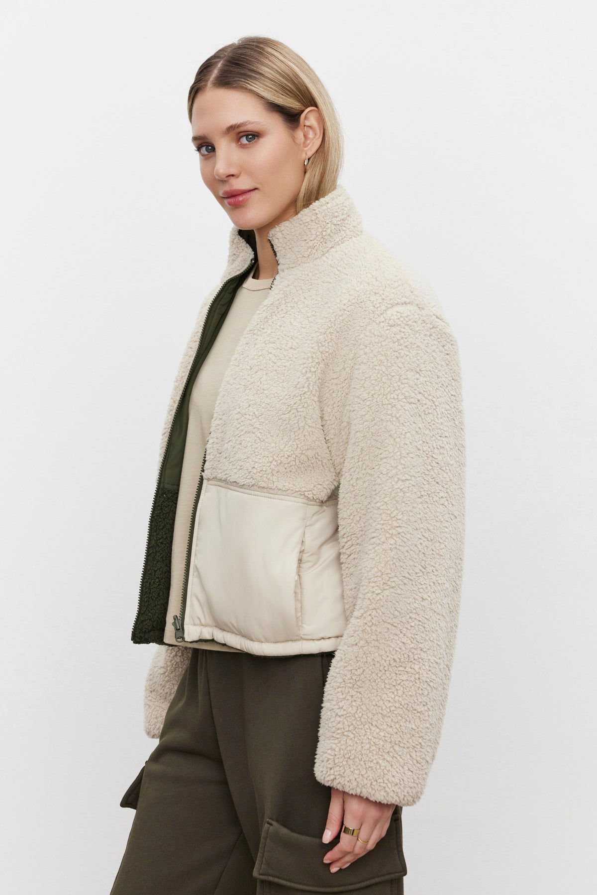 A woman with short blonde hair, dressed in a Velvet by Graham & Spencer TASHA REVERSIBLE PUFFER SHERPA JACKET over a light shirt and green cargo pants, is standing against a white background.-37676865585345