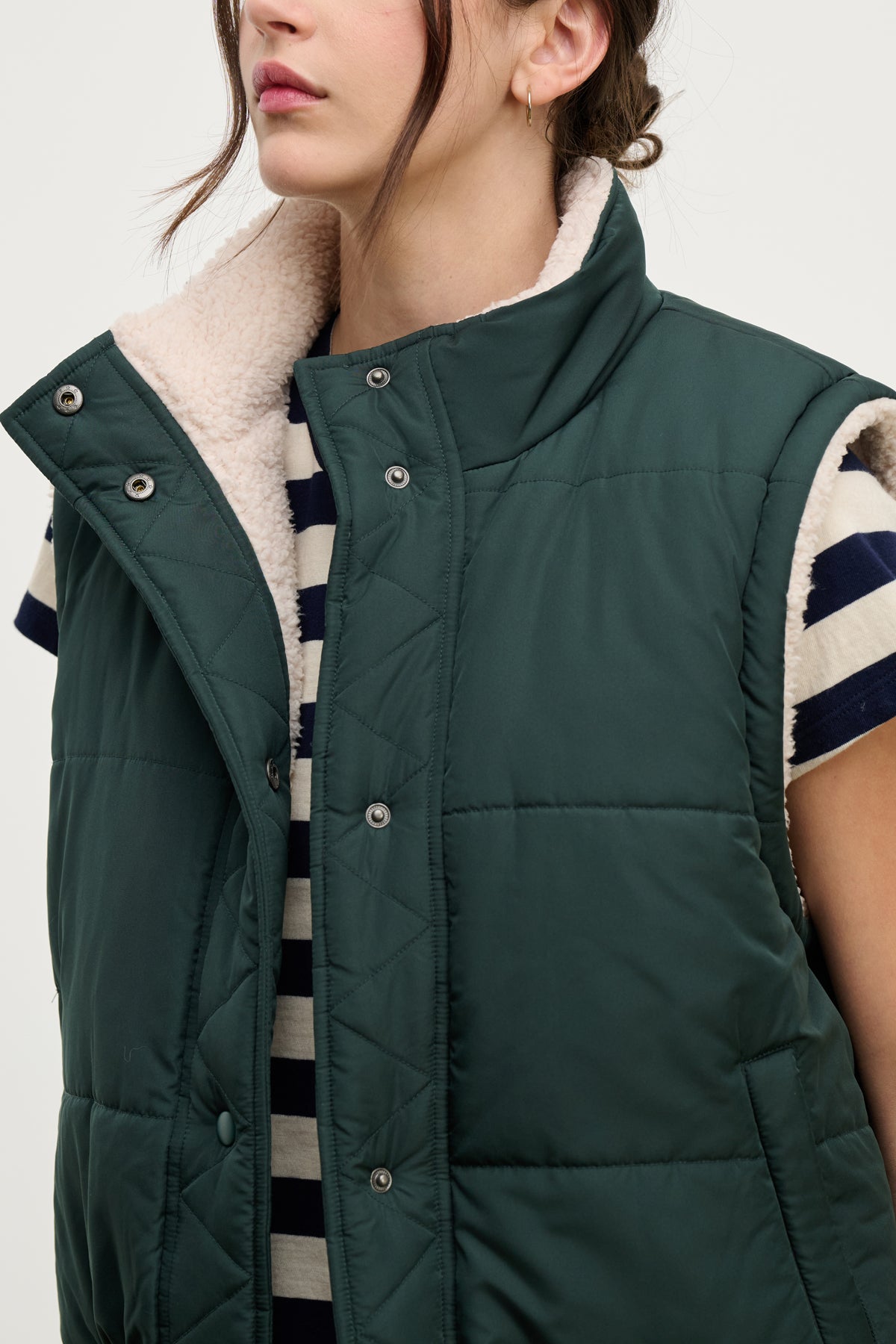 A person wears the Velvet by Graham & Spencer CATHY Puffer Sherpa Reversible Vest over a black and white striped shirt. The cozy vest, ideal for transitional layering, is unbuttoned. The person has shoulder-length brown hair.-39725321945281