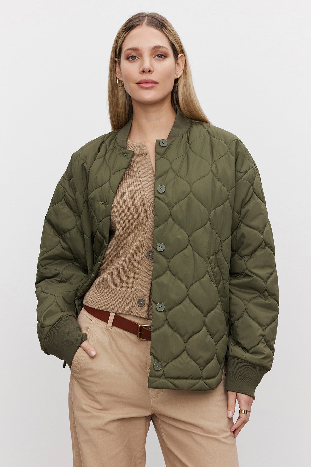   A person wearing an oversized CARIE QUILTED JACKET in green by Velvet by Graham & Spencer over a tan sweater and beige pants stands with one hand in their pocket. 