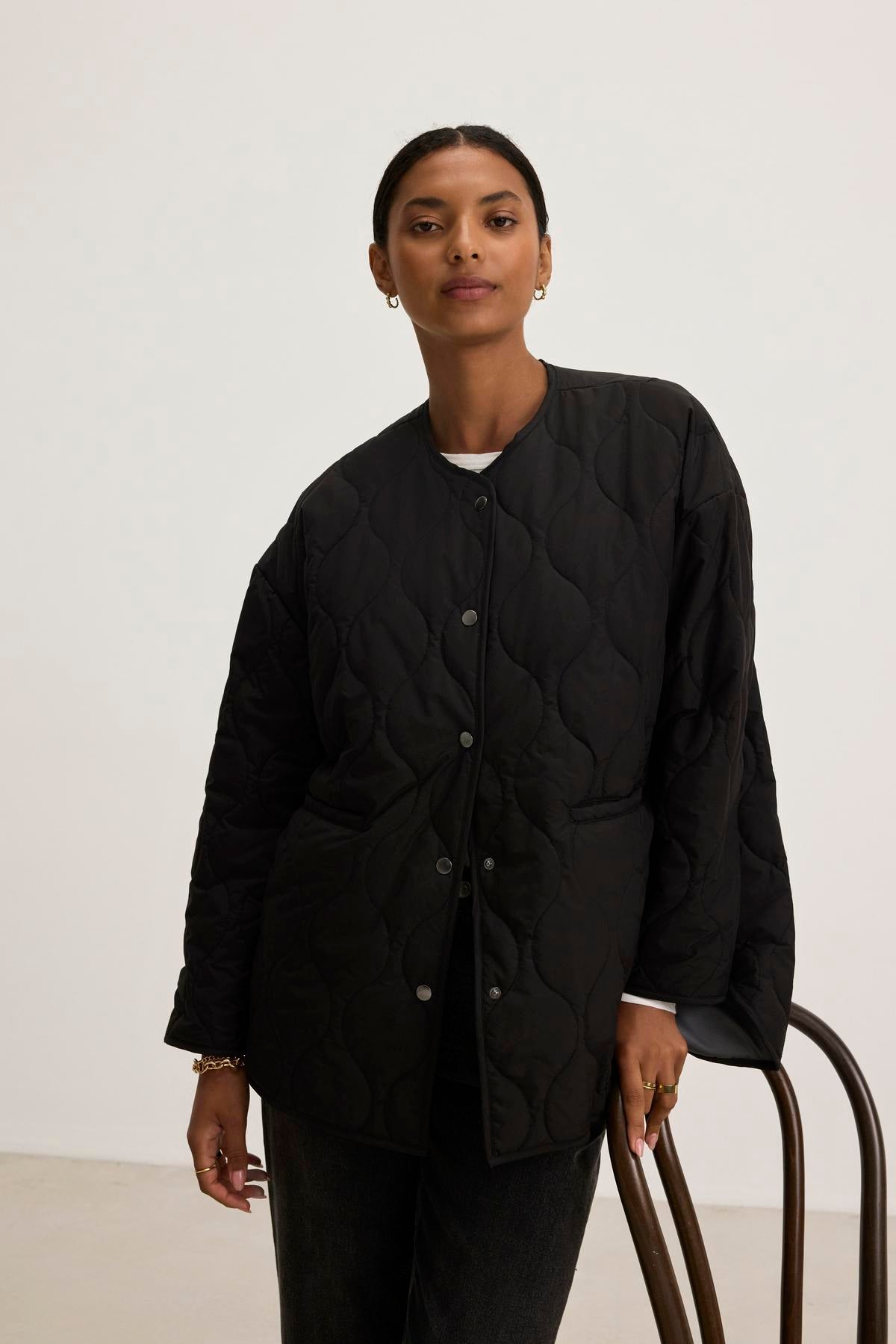   A person wearing the PAITYN QUILTED JACKET by Velvet by Graham & Spencer, which exudes vintage military jacket vibes, is standing beside a chair. 