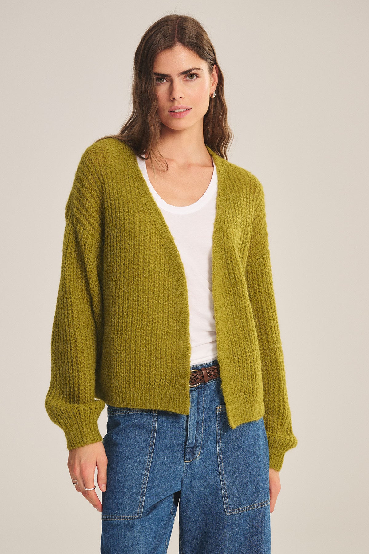 A person models the Velvet by Graham & Spencer RANYA ALPACA CARDIGAN over a white t-shirt and blue jeans, standing against a neutral background to showcase cozy layering.-39655609106625