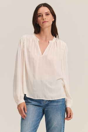 A woman wears the TAMARA BLOUSE by Velvet by Graham & Spencer, featuring a feminine ruffled neckline.
