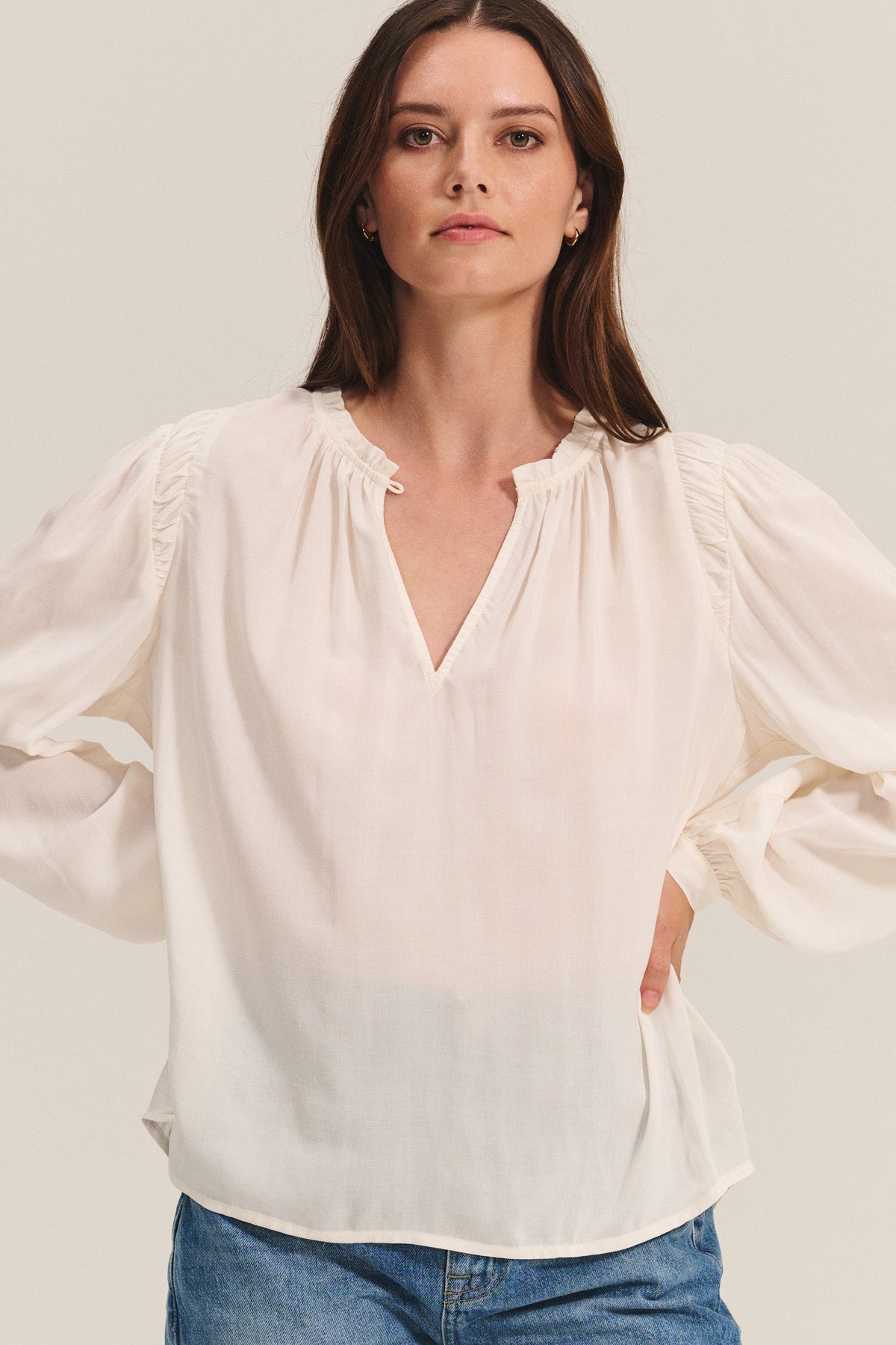 A woman faces forward in the TAMARA BLOUSE by Velvet by Graham & Spencer—a feminine rayon challis top with a v-neckline—paired with light blue jeans against a neutral background.